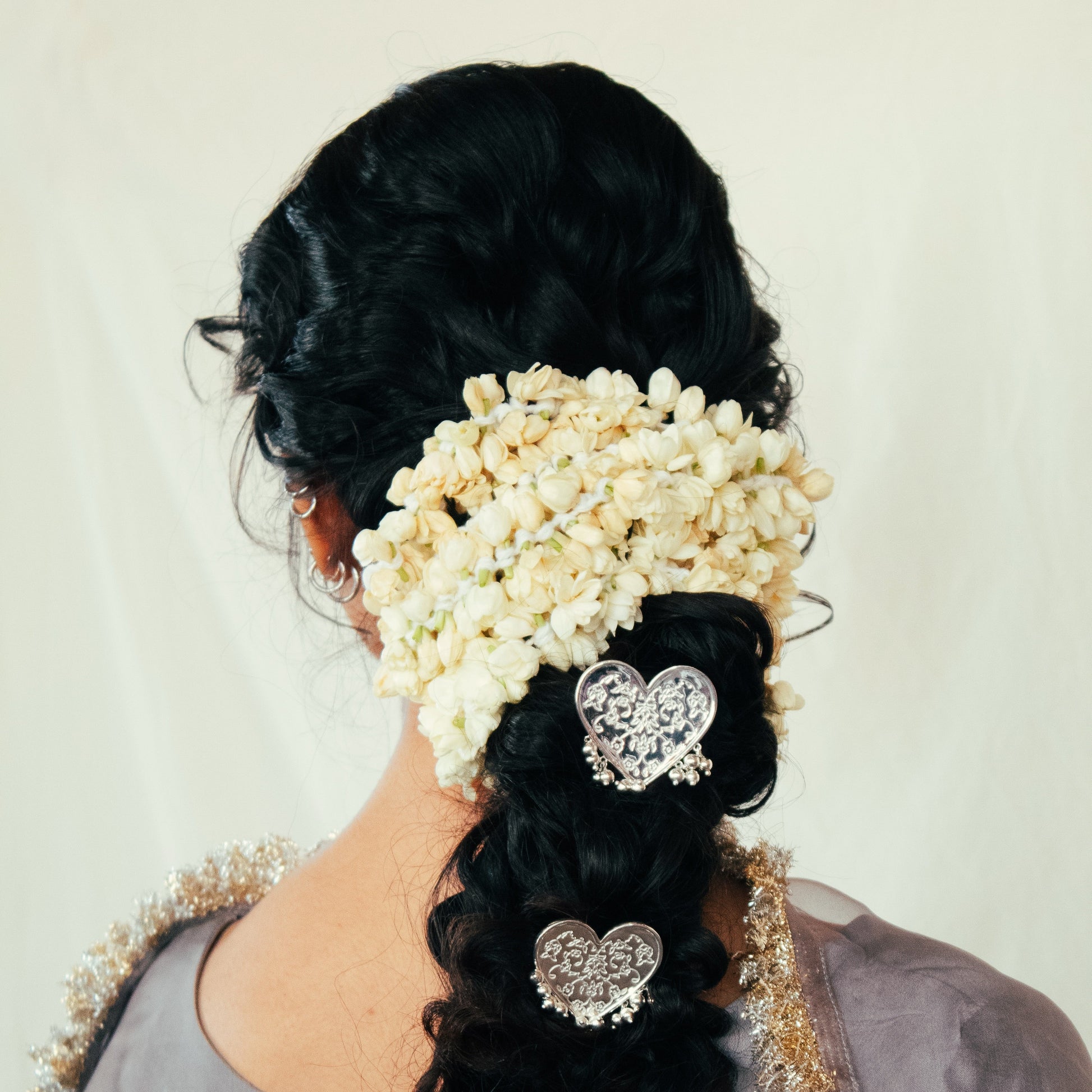 Person with braided hair adorned with decorative hairpins and flowers against a plain background