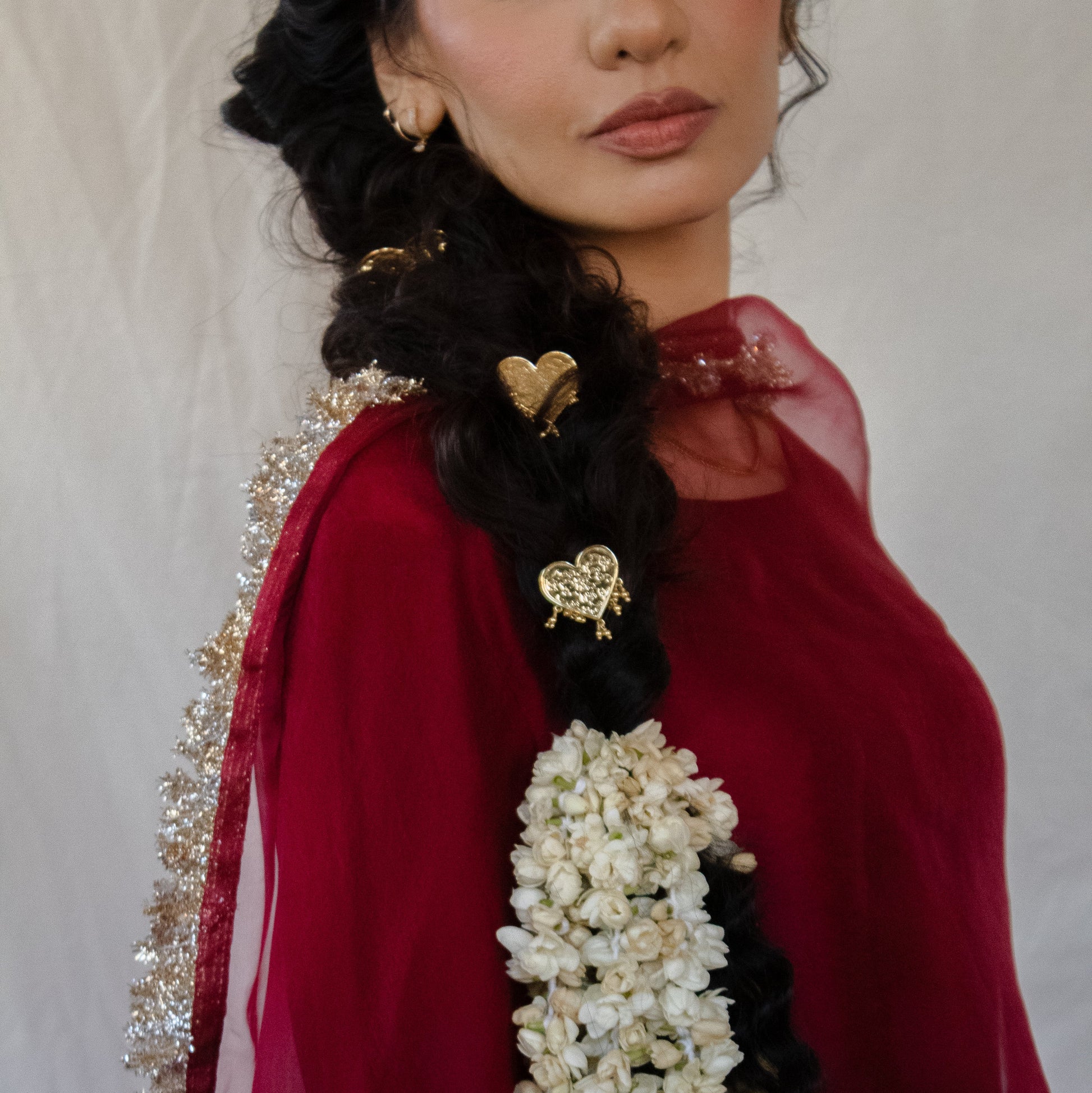 Woman wearing a red garment with a white floral garland and jewelry against a neutral background